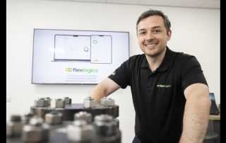 Smiling man in a black shirt standing beside industrial equipment.