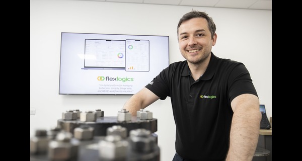 Smiling man in a black shirt standing beside industrial equipment.