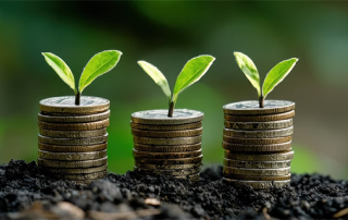 Three stacks of coins topped with small green sprouts in soil, symbolizing financial growth and investment, with a blurred green background.