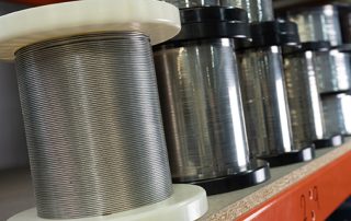 Spools of metal wire, with black and white ends, are neatly lined up on a shelf. The shiny wires suggest precision and industrial usage.