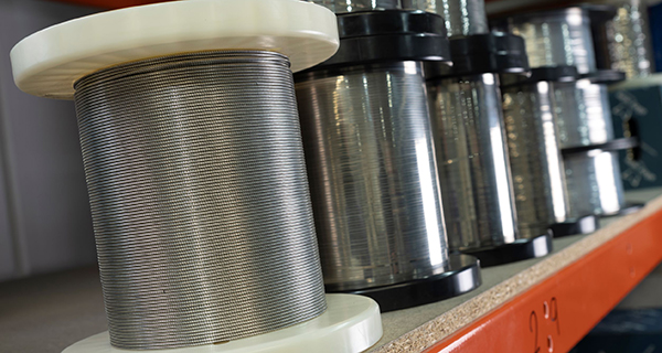 Spools of metal wire, with black and white ends, are neatly lined up on a shelf. The shiny wires suggest precision and industrial usage.