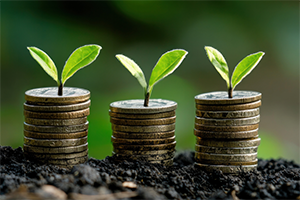 Three stacks of coins topped with small green sprouts in soil, symbolizing financial growth and investment, with a blurred green background.